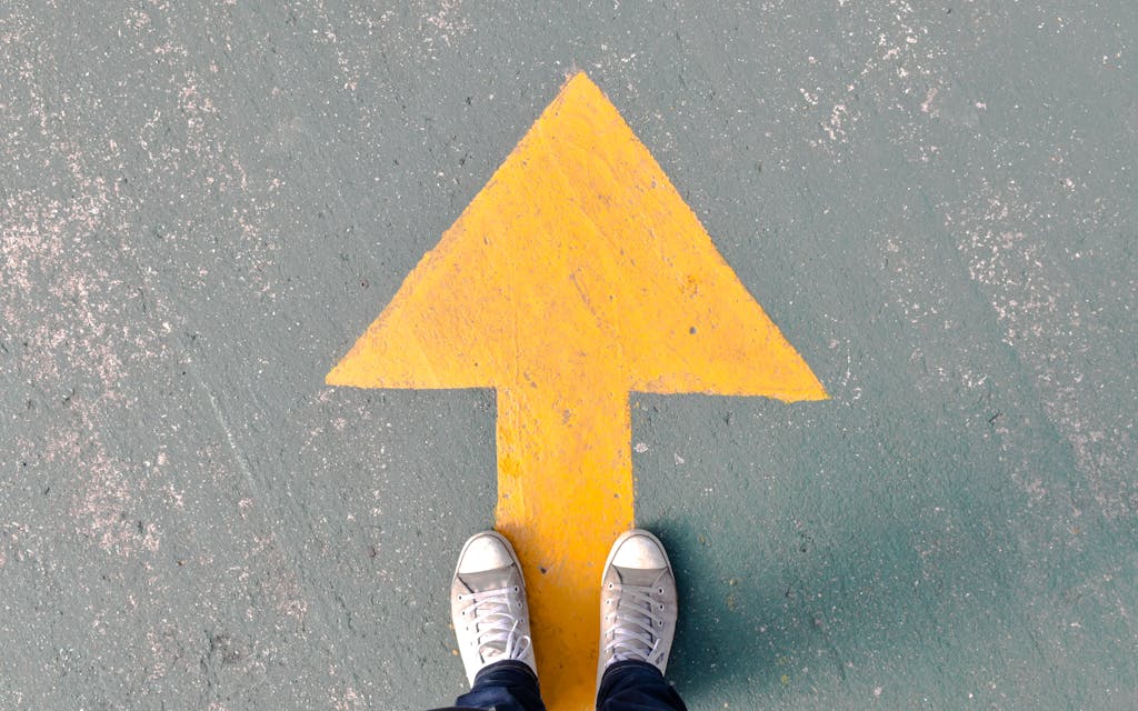 Top view of shoes standing on asphalt with a yellow directional arrow.